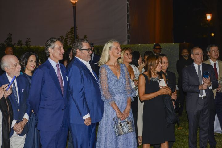 Un grupo de personas vestidas de gala posan en un evento nocturno en un jardín